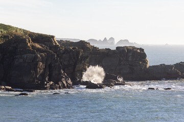 A rocky shoreline with a large wave crashing into the rocks