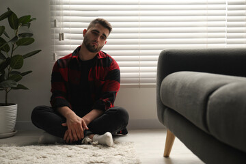 Sad man sitting near closed blinds indoors