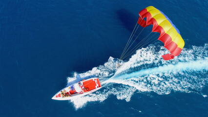 People fly on parachute attached to motorboat with group of tourists at summer sunny day. Aerial...