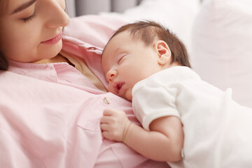 Mother with her sleeping newborn baby on bed, closeup