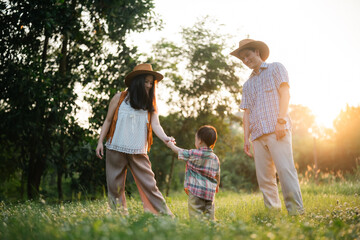 Asian family of three, a man, a woman and a child, are walking through a grassy field, summer activity in nature park is happy fun outdoor lifestyle