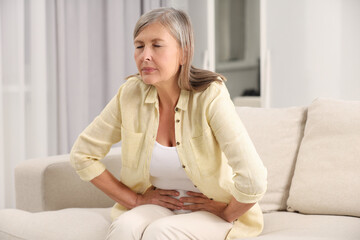 Menopause. Woman suffering from abdominal pain on sofa at home