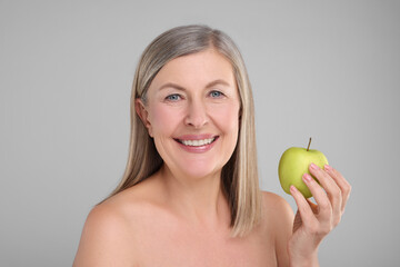 Beautiful woman with fresh apple on grey background. Vitamin rich food