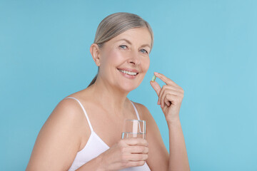 Beautiful woman with vitamin capsule and glass of water on light blue background