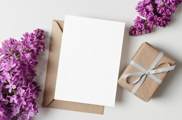 Blank greeting card mockup with gift box and lilac flowers, flat lay card with copy space