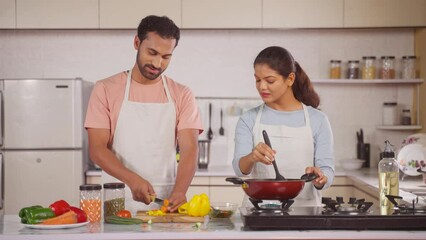 joyful happy married Indian couples cooking together at kitchen during weekend - concept of relationship bonding and partner assistance or support.
