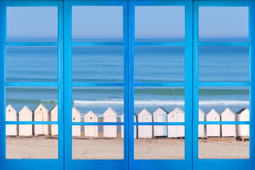Blue window with a view on a beach with vintage white cabins - 755756698