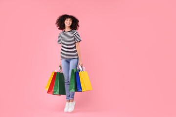 Happy young woman with shopping bags on pink background