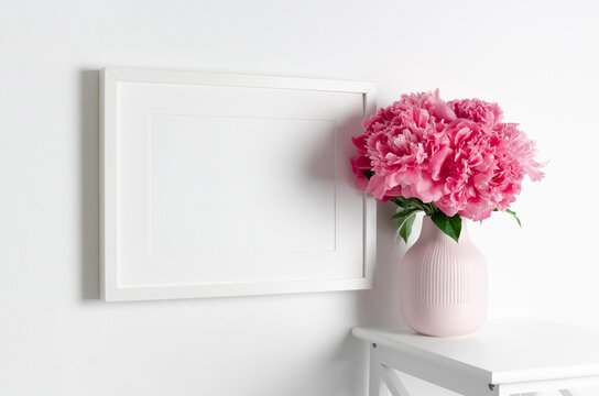 White frame mockup on wall with pink peony flowers bouquet for artwork, photo or print presentation