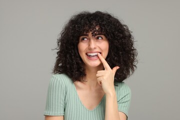 Fototapeta na wymiar Young woman applying whitening strip on her teeth against grey background