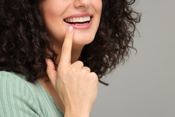Young woman showing her teeth with whitening strip on grey background, closeup. Space for text