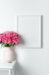 White portrait picture frame mockup on white wall, blank frame mock up with pink peony flowers