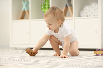 Children toys. Cute little boy playing with wooden car on rug at home