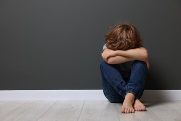 Child abuse. Upset boy sitting on floor near grey wall, space for text
