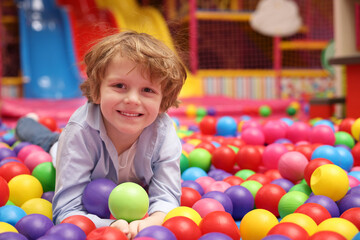 Fototapeta na wymiar Happy little boy lying on colorful balls in ball pit, space for text