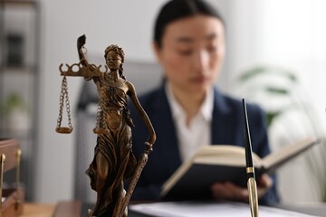 Notary reading book at table in office, focus on statue of Lady Justice and pen - obrazy, fototapety, plakaty
