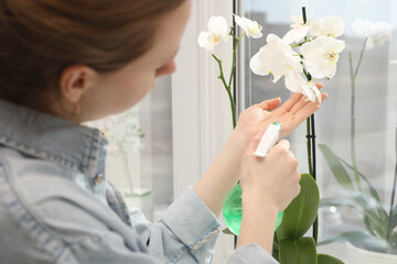 Woman spraying blooming orchid flowers with water near window, closeup