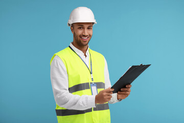 Engineer in hard hat holding clipboard on light blue background