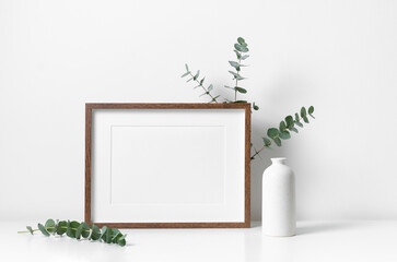 Horizontal picture frame mockup in white minimalistic scandinavian interior with fresh eucalyptus...