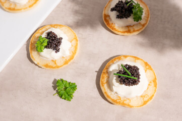 Blinis or mini pancakes with black caviar and sour cream, seafood appetizer.
