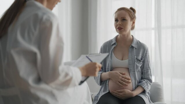 Pregnant woman consulting with a doctor. Smiling young pregnant woman patient answers gynecologist questions at hospital, medical clinic. Doctor examine pregnant belly check up. Gynecology concept.