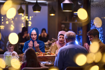 Fototapeta na wymiar In a modern restaurant setting, a European Islamic family comes together for iftar during Ramadan, engaging in prayer before the meal, uniting tradition and contemporary practices in a celebration of