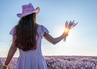 Girl walking in the lavender field and holding lavender bouquet in her hand. Brihuega, Spain. - 755782466