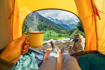 Cup of hot drink in the hand and wonderful view of snowy mountain tops through the open entrance of the tent. The beauty of a romantic hike and camping accompanied by a dog. - 755783408