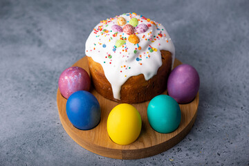 Easter kulich with candied fruits in white glaze with colorful sprinkles and painted eggs. Traditional Easter pastry. Easter holiday. Close-up, selective focus.