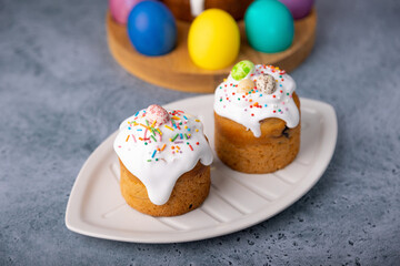 Two small Easter kulichs with candied fruits in white glaze with colorful sprinkles in the cut. Painted chicken and quail eggs. Traditional Easter baking. Easter holiday. Close-up, selective focus.