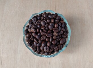 Coffee beans in a glass bowl on a wooden table.
