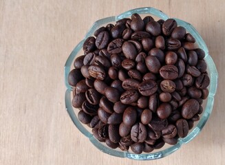 Coffee beans in a glass bowl on a wooden table.