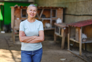 Adult woman farmer with white rabbits in her farm. The farmer takes care of the animals
