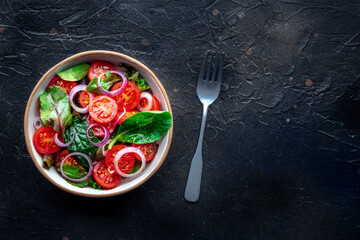 Salad with tomato, fresh leaves, and onions, overhead flat lay shot. Healthy diet, simple vegan recipe, on a black slate background, with copy space - 755792447