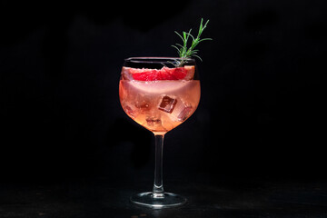 Fancy cocktail with fresh fruit. Gin and tonic drink with ice at a party, on a black background. Alcohol with pink grapefuit and rosemary - 755792871