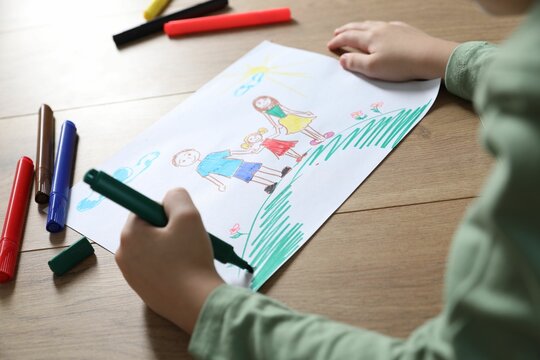 Little boy drawing picture with marker at wooden table, closeup. Child`s art