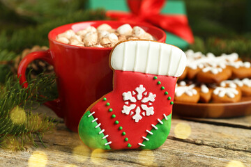 Tasty cookie in shape of Christmas stocking, cocoa with marshmallows and fir tree branch on wooden...