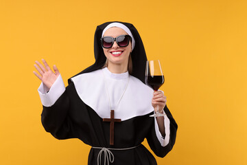 Happy woman in nun habit and sunglasses holding glass of wine against orange background. Sexy...
