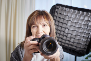 Senior old elderly woman with black camera with a large lens indoors in the studio. A professional photographer. Age Hobby