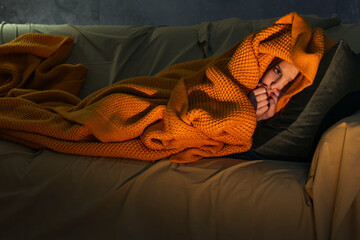 Little girl hiding from monster in blanket on sofa at night