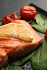 Tasty grilled salmon with lemon, spinach and tomatoes on table, closeup