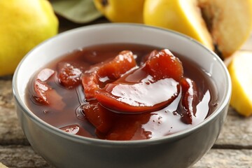 Tasty homemade quince jam in bowl on wooden table, closeup
