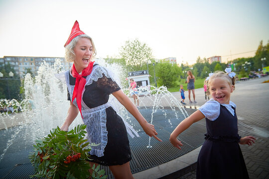 Young and adult schoolgirl on September with flowers having fun near water of fontain. Generations of schoolchildren, pioneer of USSR and October girl in modern uniform of Russia. Mother and daughter