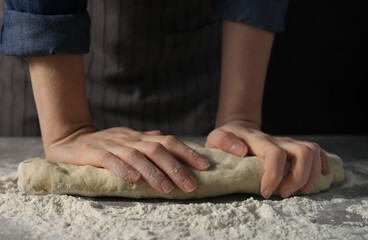 Obraz na płótnie Canvas Making bread. Woman kneading dough at table on dark background, closeup
