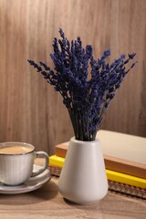 Bouquet of beautiful preserved lavender flowers, notebooks and cup of coffee on wooden table indoors