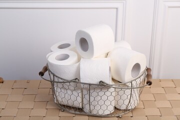 Soft toilet paper rolls in metal basket on wicker table, closeup