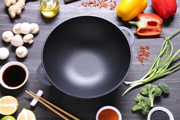 Empty iron wok and chopsticks surrounded by ingredients on dark grey wooden table