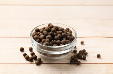 Dry allspice berries (Jamaica pepper) in bowl on light wooden table