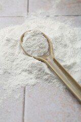 Pile of baking powder and spoon on light tiled table, closeup