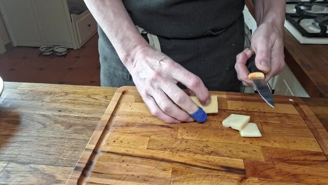 The chef cuts the cheese into cubes. Man's hands cut cheese into cubes. Chef's finger bandaged with a plaster. Concept of cooking, gastronomy and culinary. Footage from home kitchen